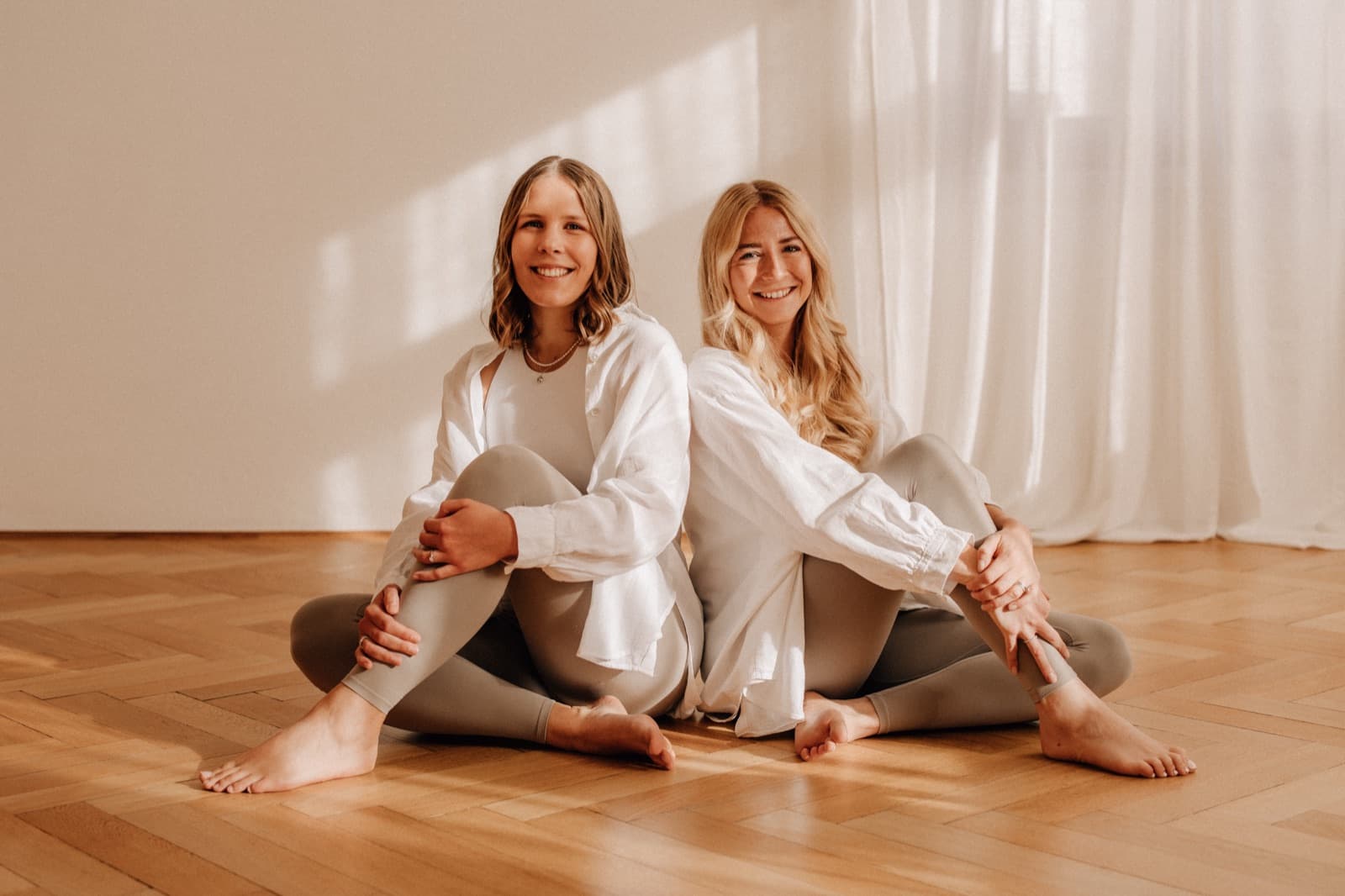 Sara und Céline sitzen Rücken an Rücken im Yogastudio