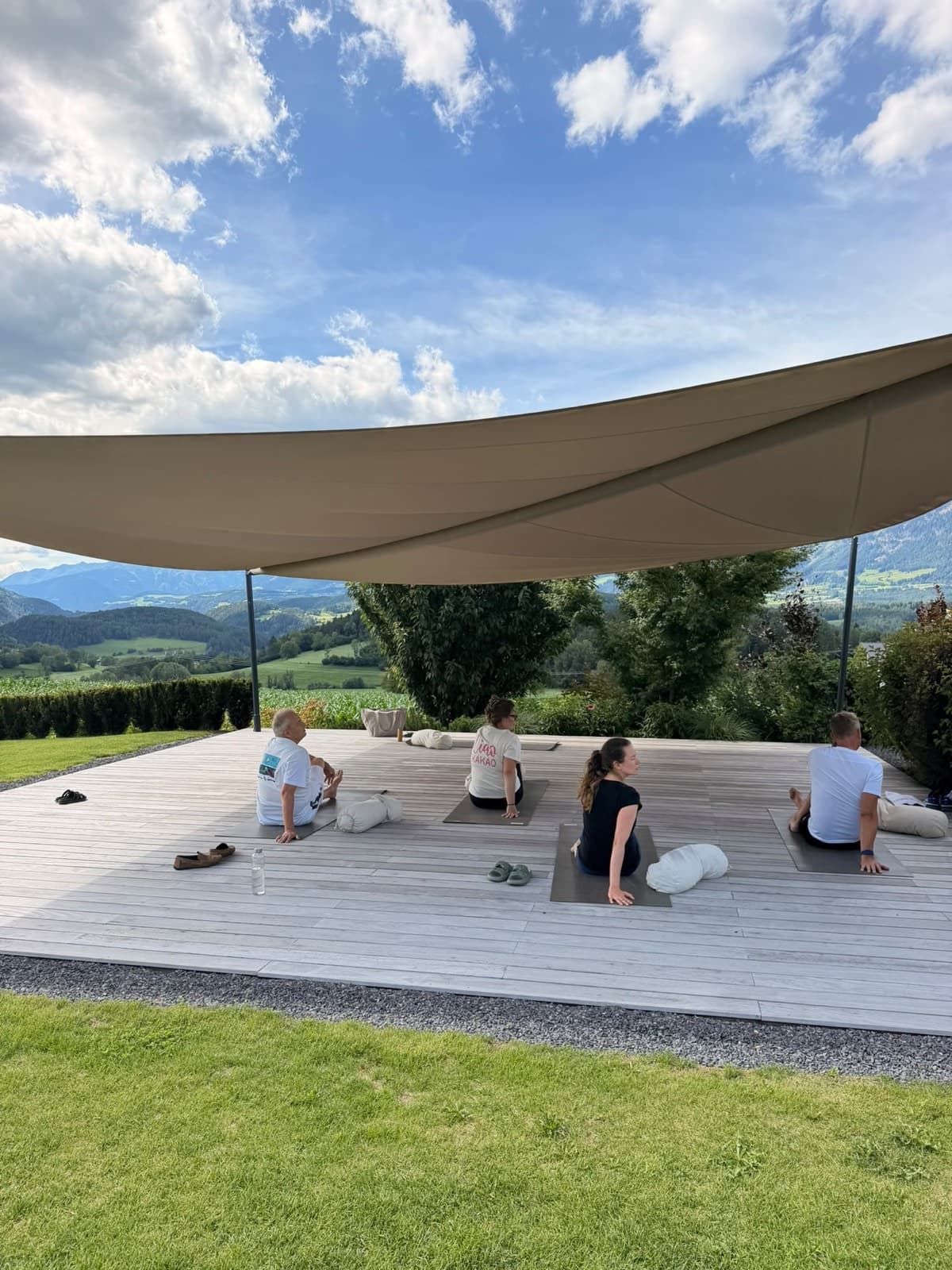 Yogagruppe unter einem Sonnensegel mit Bergpanorama